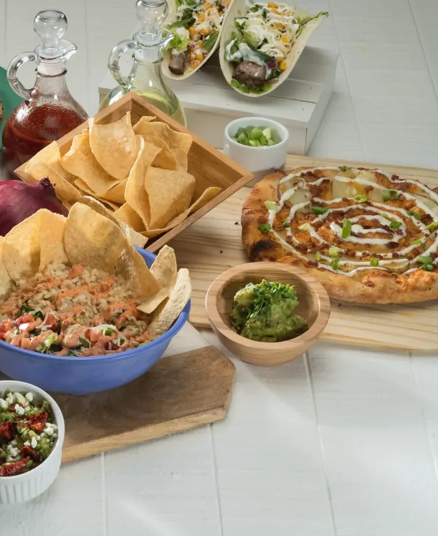 Chips and a bowl of rice and salsa beside a bacon-and-ranch pizza and a bowl of guacamole