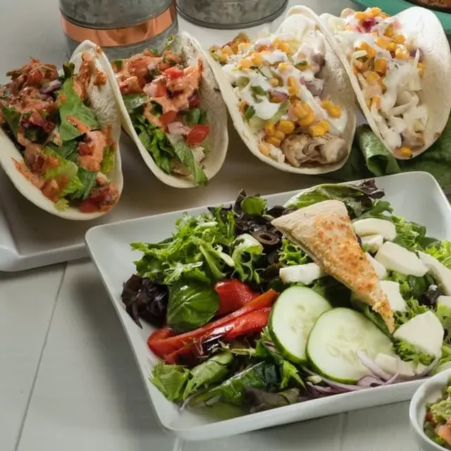 Four flour tacos beside a green salad with mozzarella and cucumber